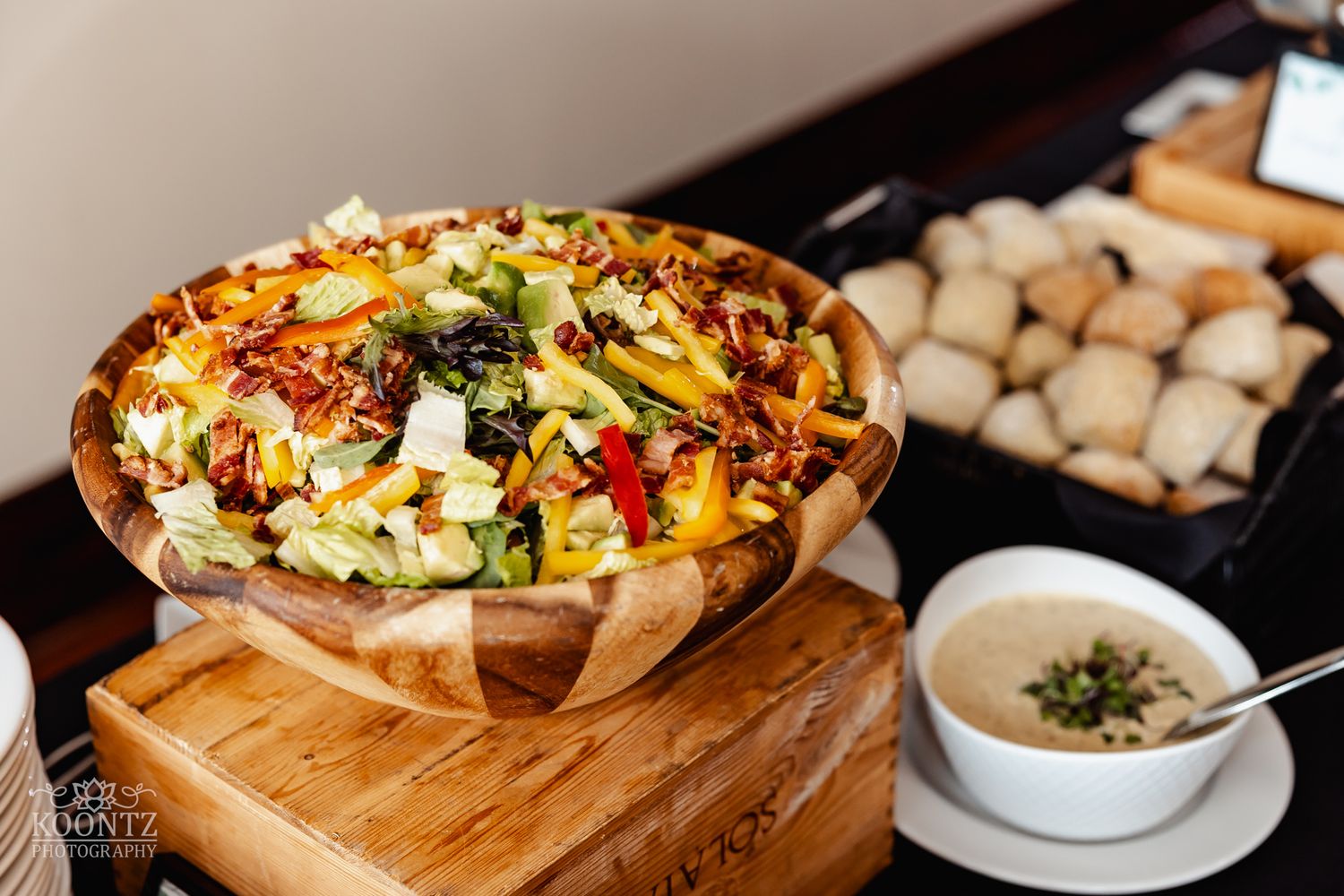 Colorful salad topped with vegetables and cheese served in wooden bowl with side of creamy soup.