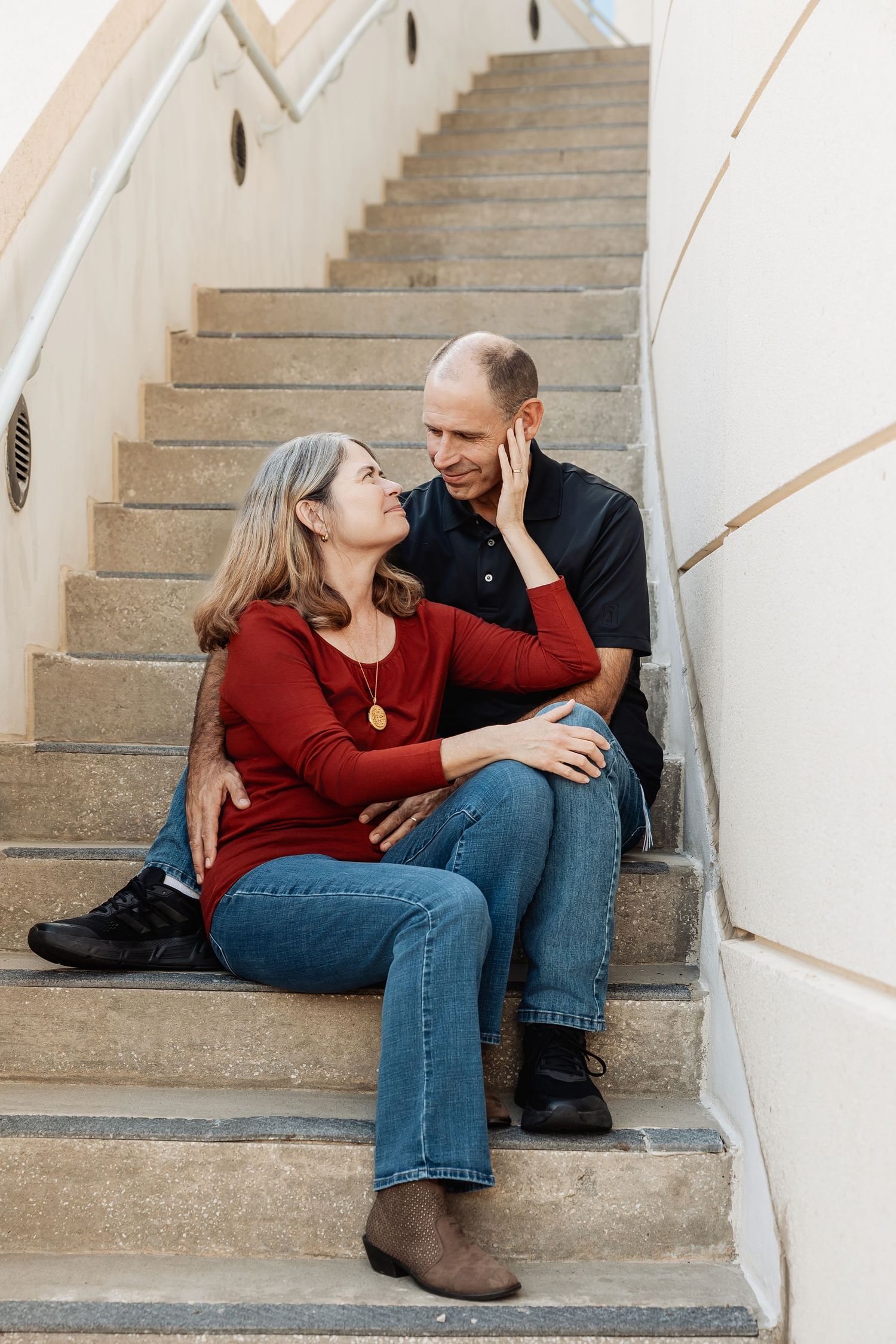 Couple sharing a tender moment on outdoor stairs, woman in red top touching mans face gently.