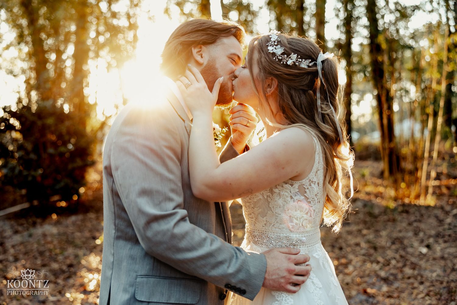 Bride and groom share a kiss in golden sunlight among autumn trees at their outdoor rustic wedding.
