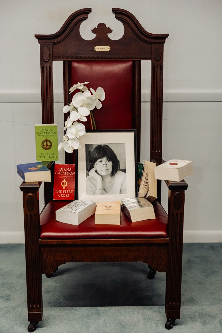 An ornate wooden chair with red upholstery displays books and a white orchid.