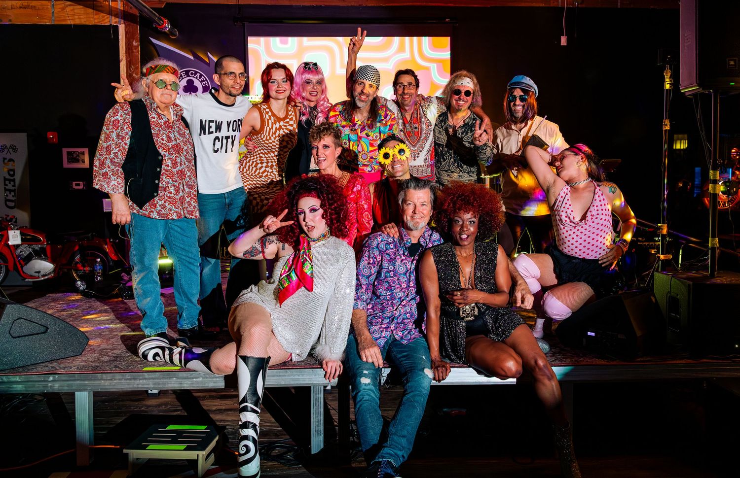Diverse group of colorfully dressed performers posing together on stage after a vibrant live show.