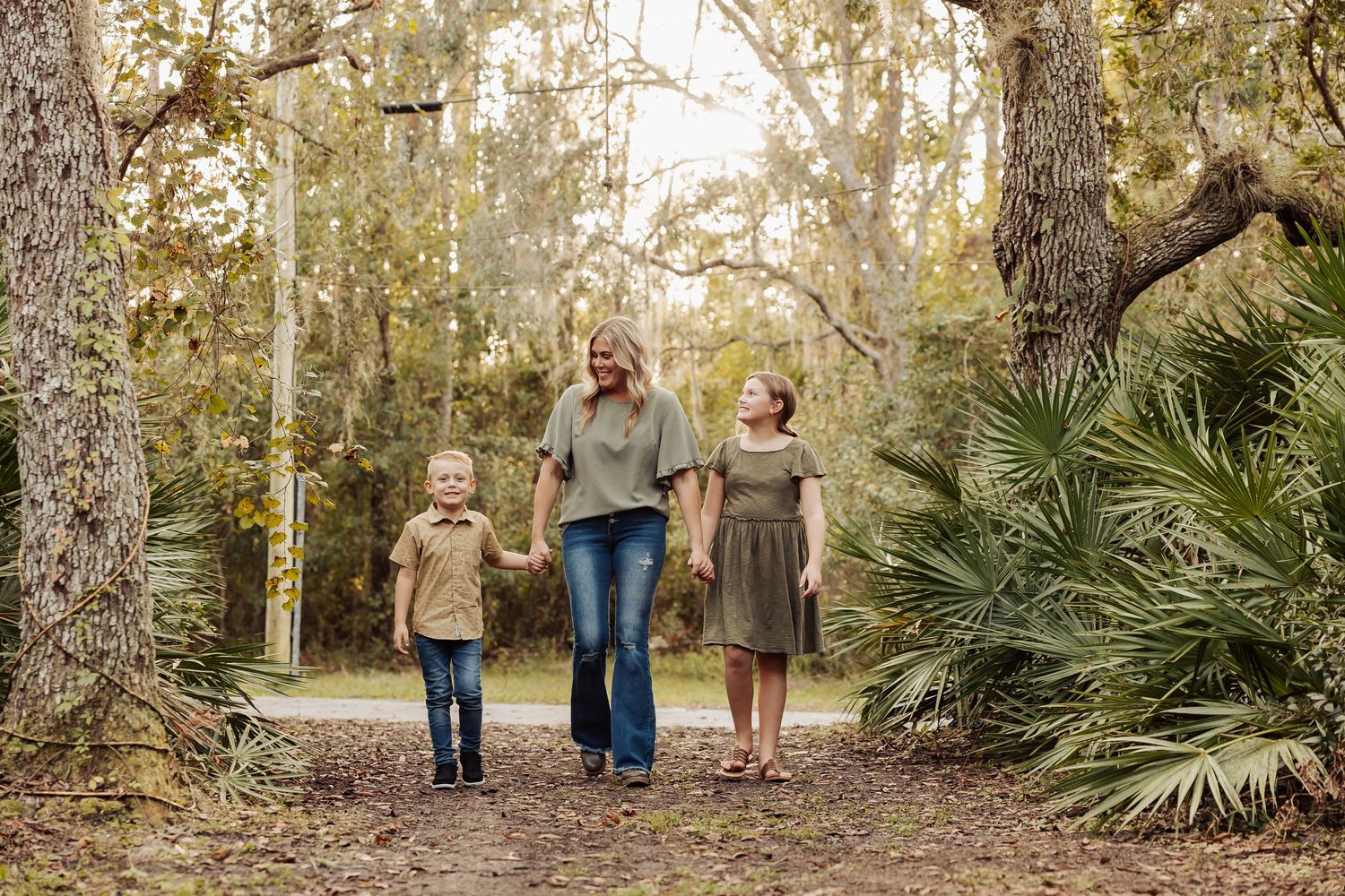 A mother walks hand-in-hand with her two children along a wooded forest path.
