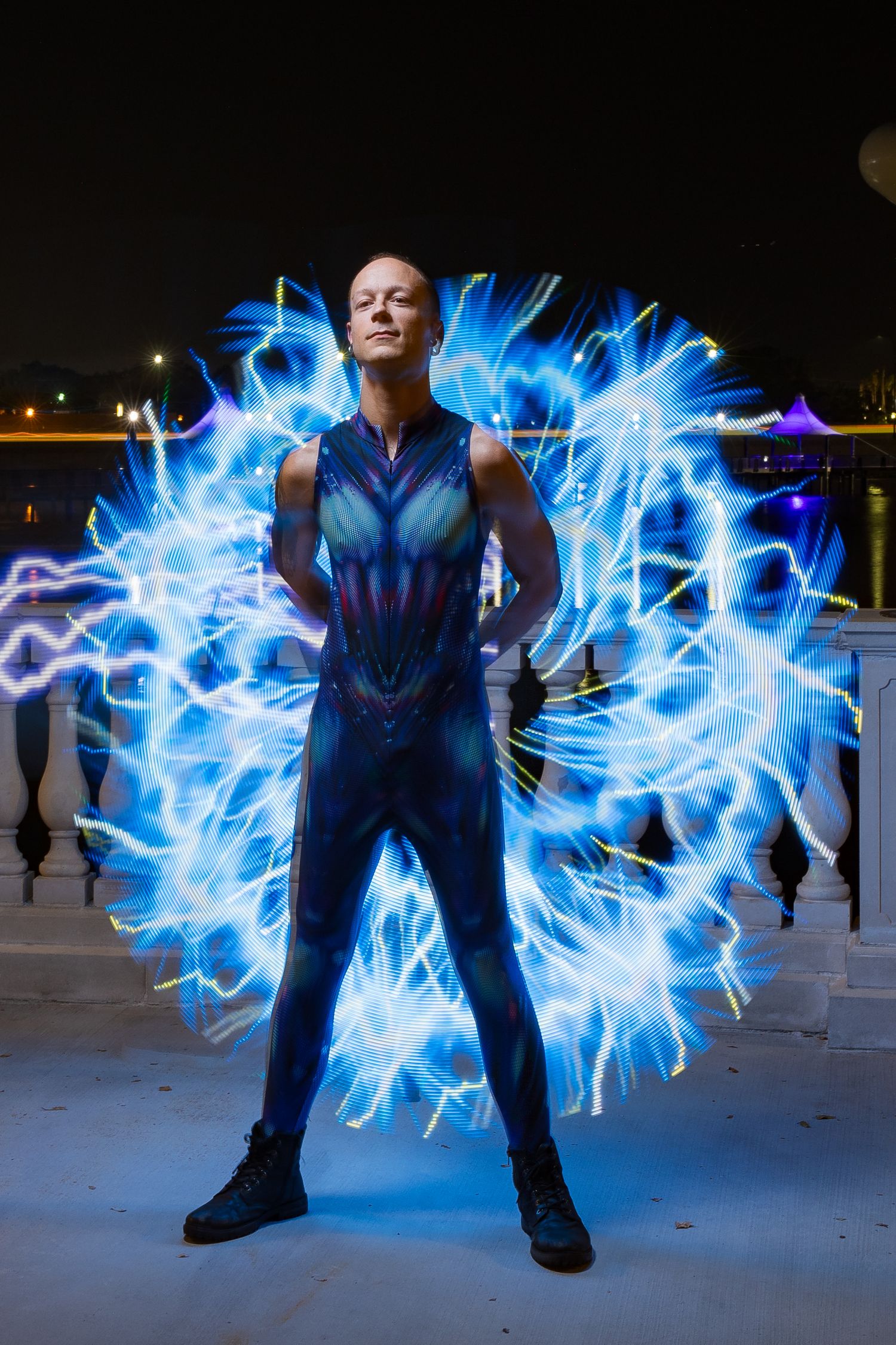 Bald man in blue superhero suit stands surrounded by electric blue light orb at night.