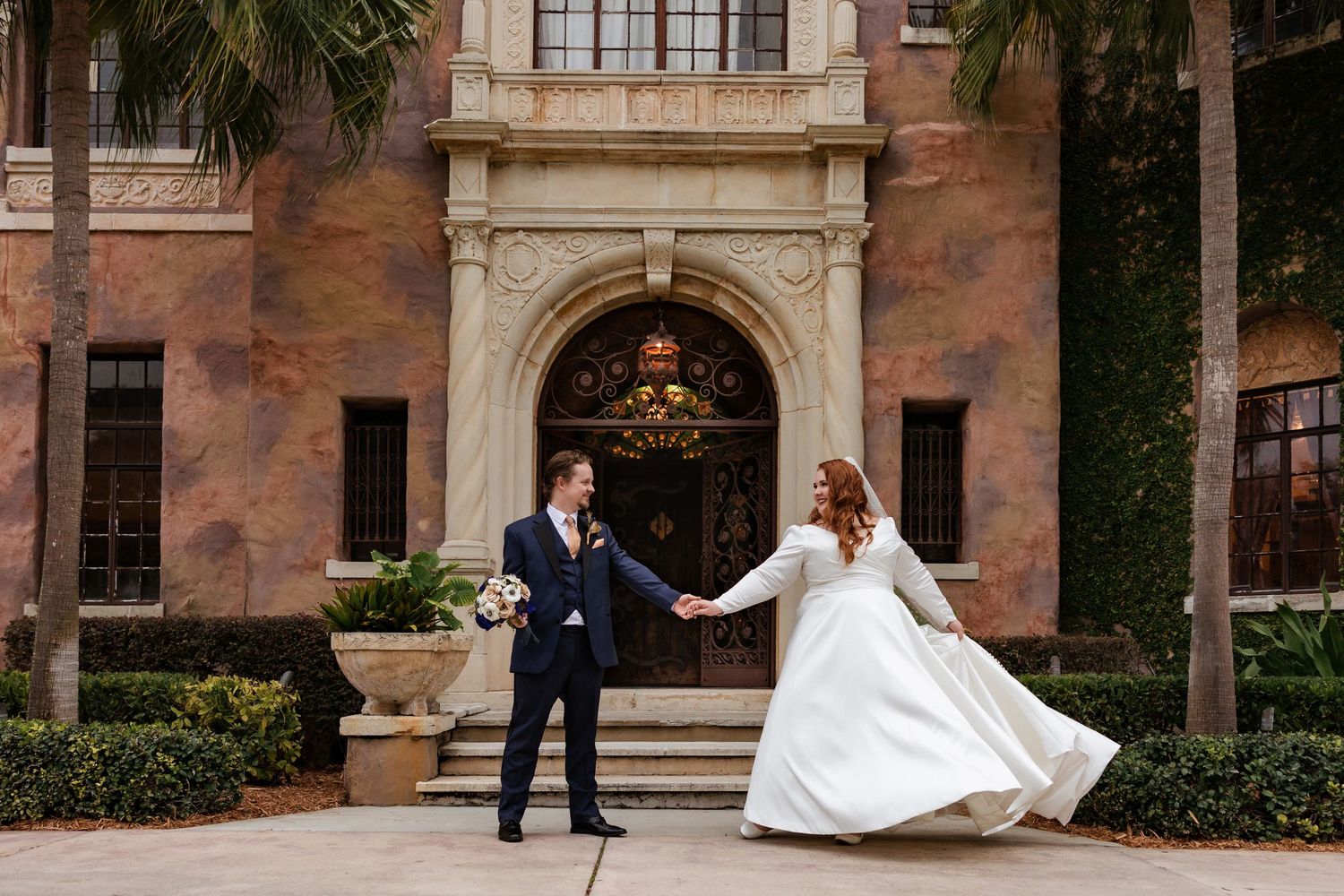 Bride and groom holding hands outside elegant historic wedding venue.