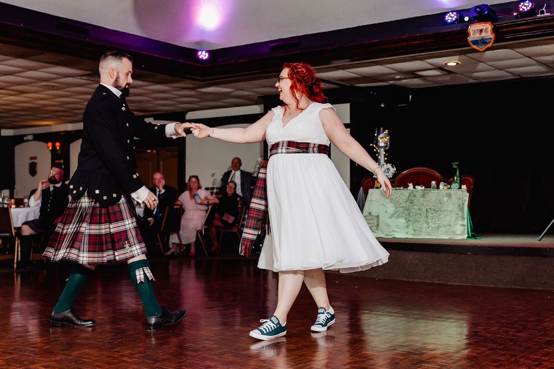Dancers in traditional Scottish attire performing on a wooden dance floor.