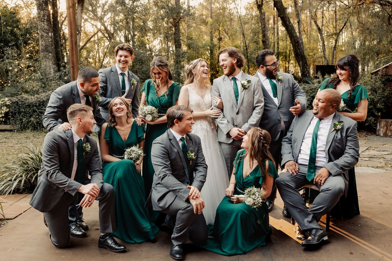 Wedding party in emerald dresses and grey suits lounging casually outdoors.