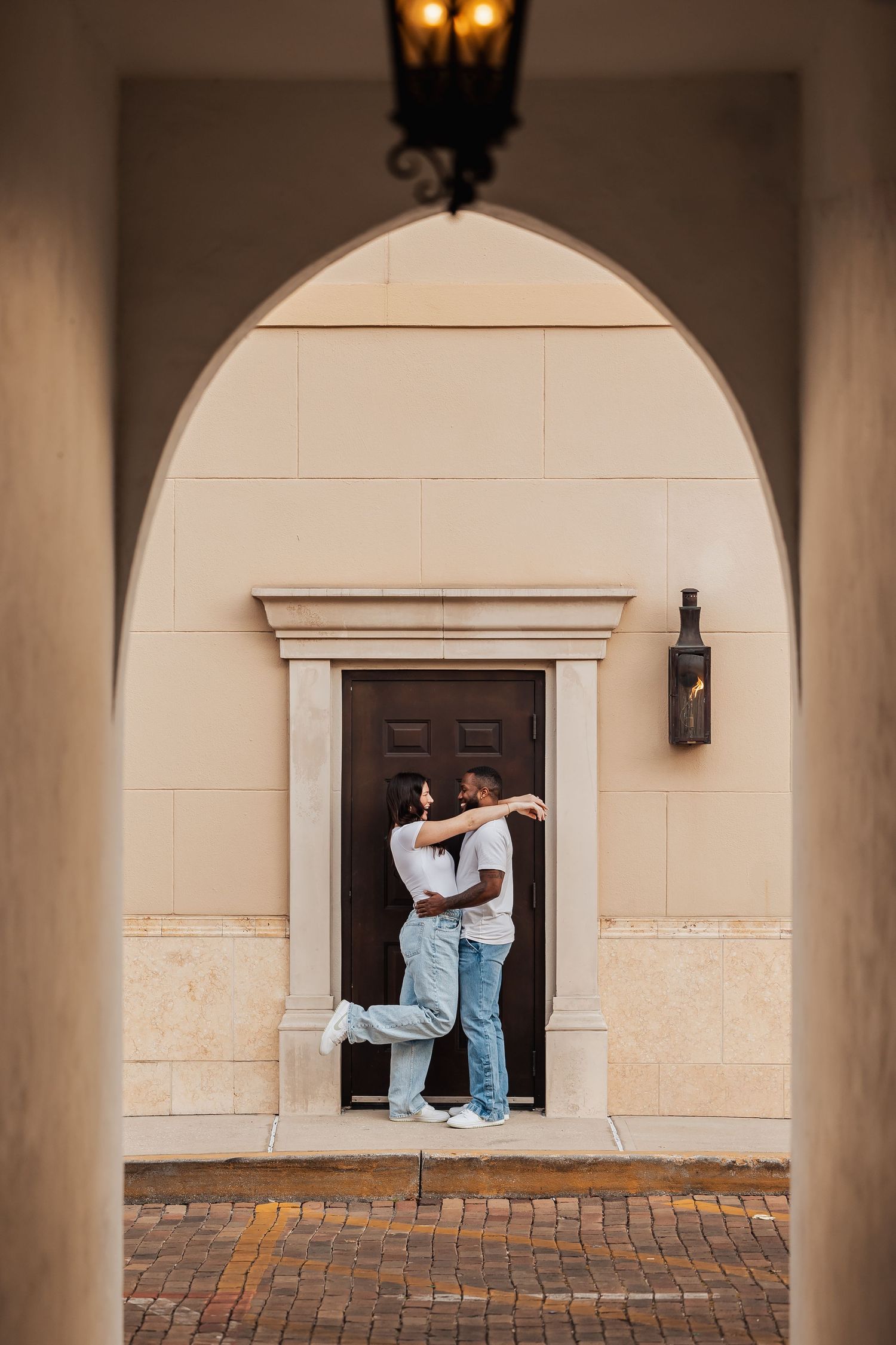 A couple embraces in a doorway framed by an arched Mediterranean-style entryway.