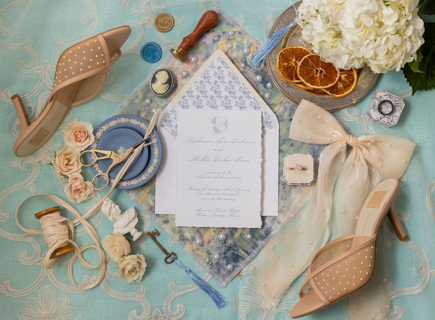 Wedding details flatlay with invitation, shoes, flowers and accessories on blue background.