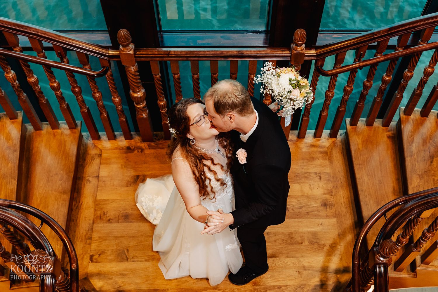 Intimate wedding portrait on wooden staircase with warm lighting and ornate railings.