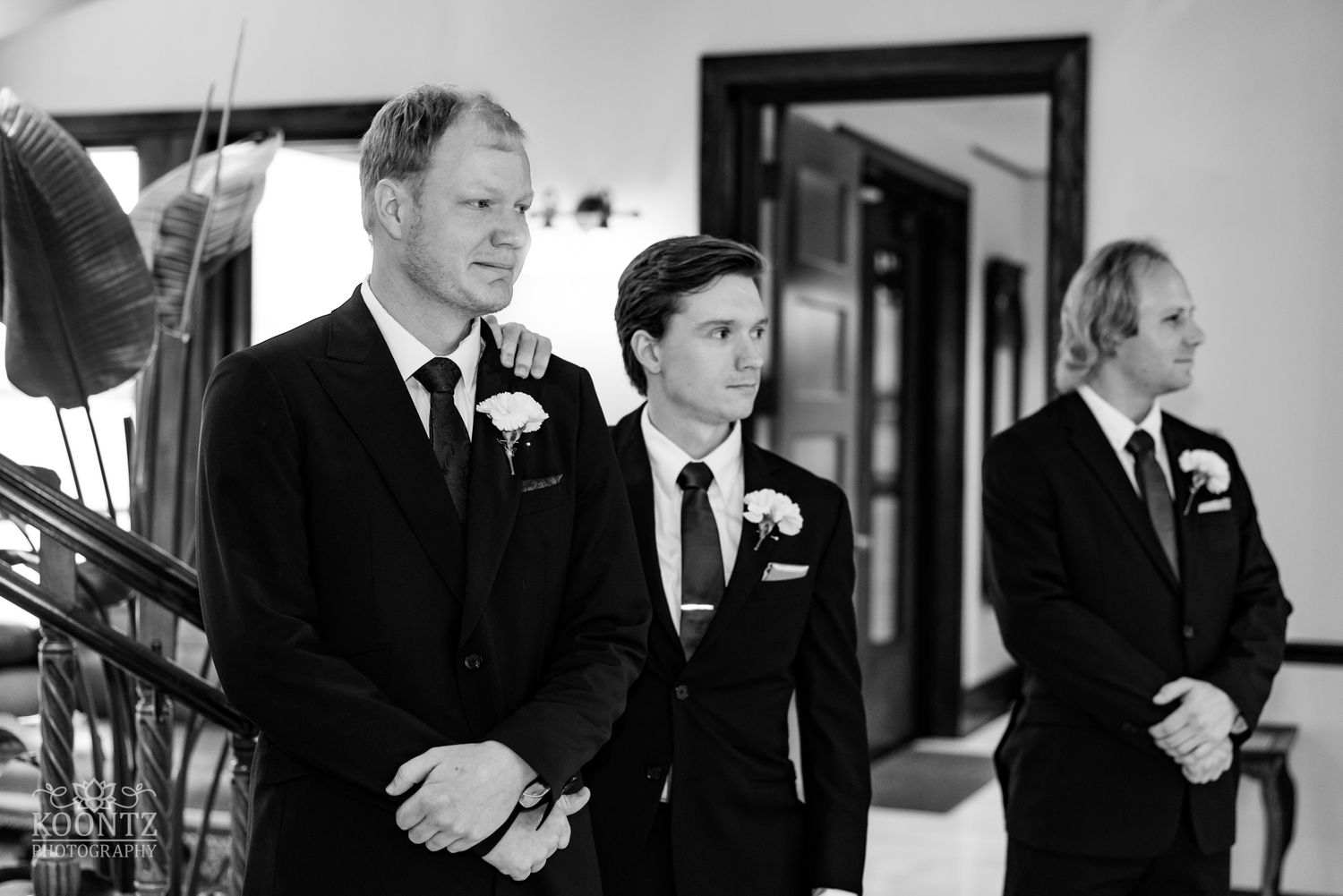 Groomsmen wait expectantly during wedding ceremony in formal black suits.