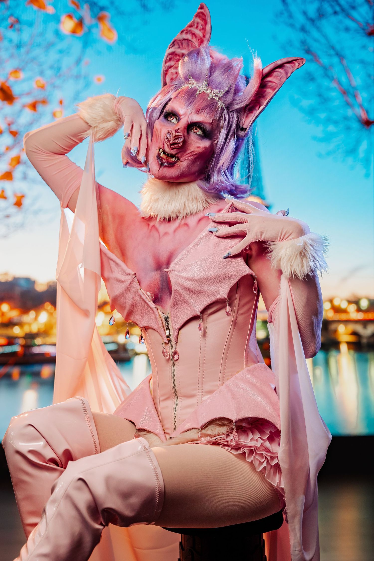 Pink fantasy costume photoshoot with butterfly ears against blue twilight cityscape.