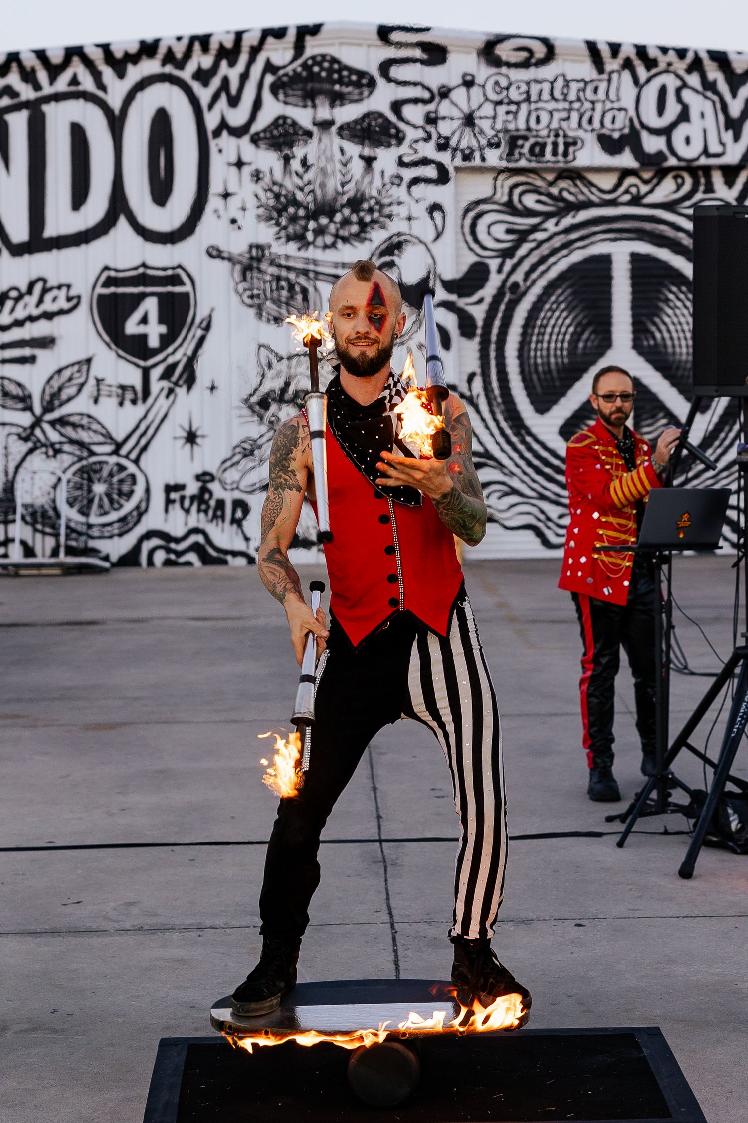 Tattooed fire juggler in red vest performing with flaming props at the Central Florida Fair event.