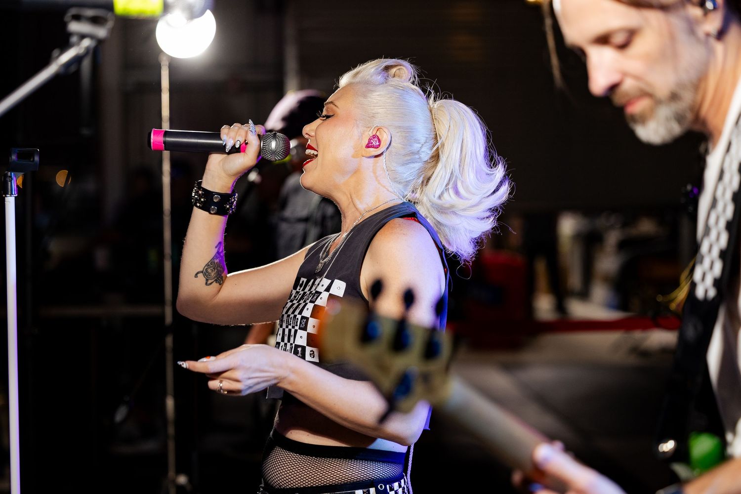 Close-up of blonde female rock vocalist singing passionately on stage with guitarist in foreground.