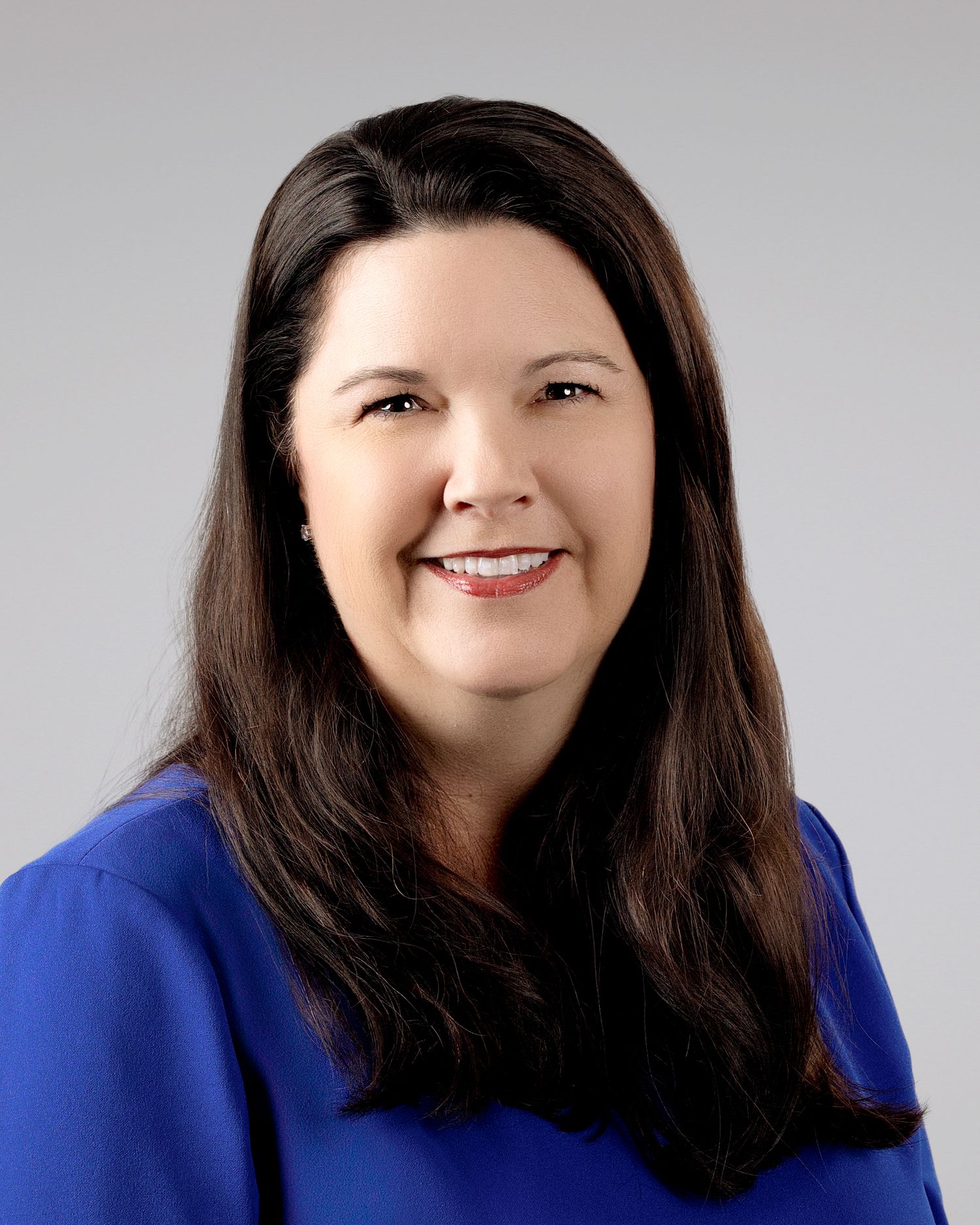 Professional headshot of a smiling woman with long brown hair wearing a blue top.