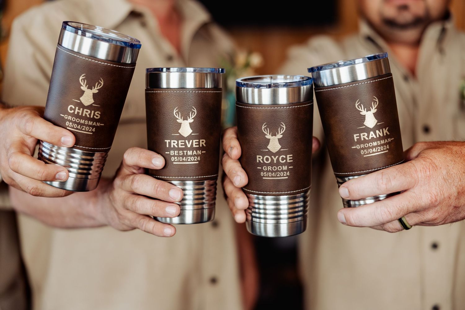 Four brown insulated tumblers with deer logos being held together in a toast.