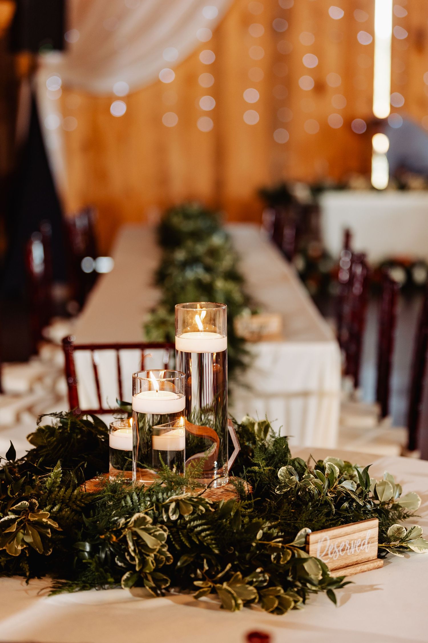 Elegant wedding table centerpiece with floating candles and lush greenery garland.