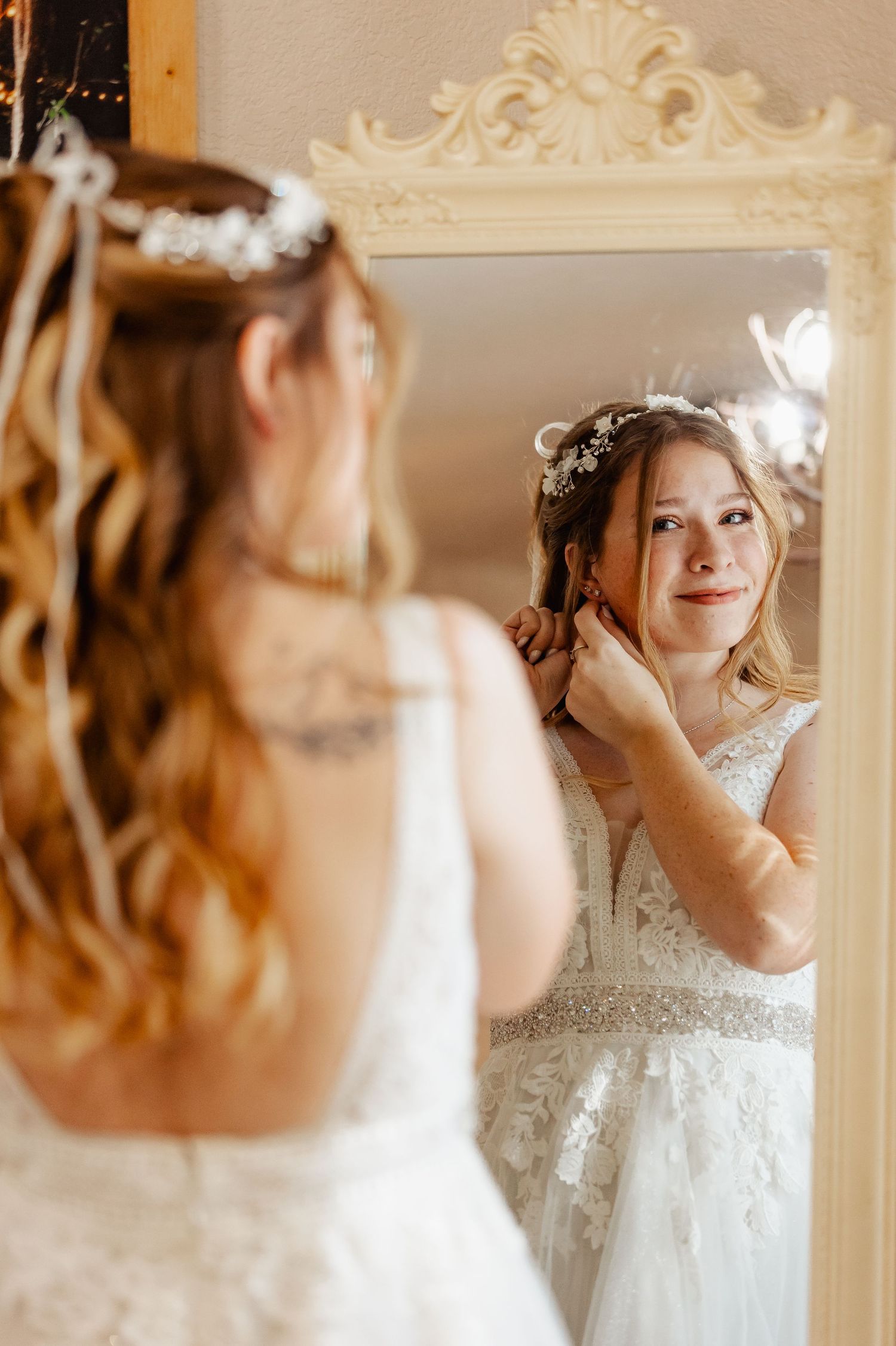 Reflection in ornate mirror shows bride adjusting hair accessory.