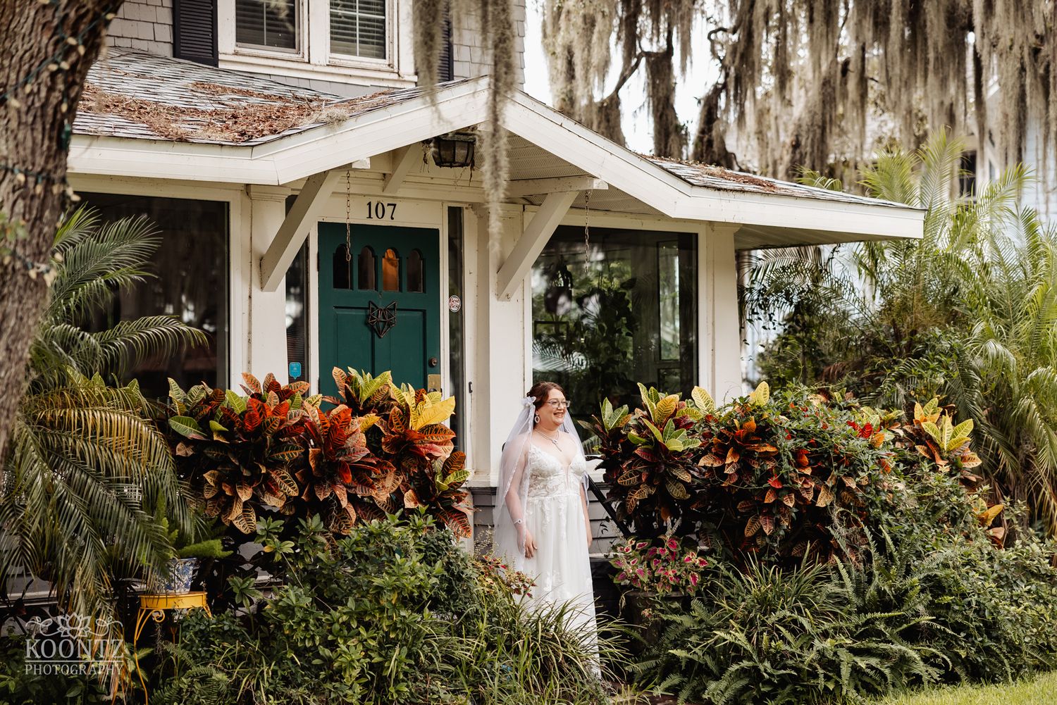 Bride in white dress standing outside charming cottage with tropical garden and Spanish moss.
