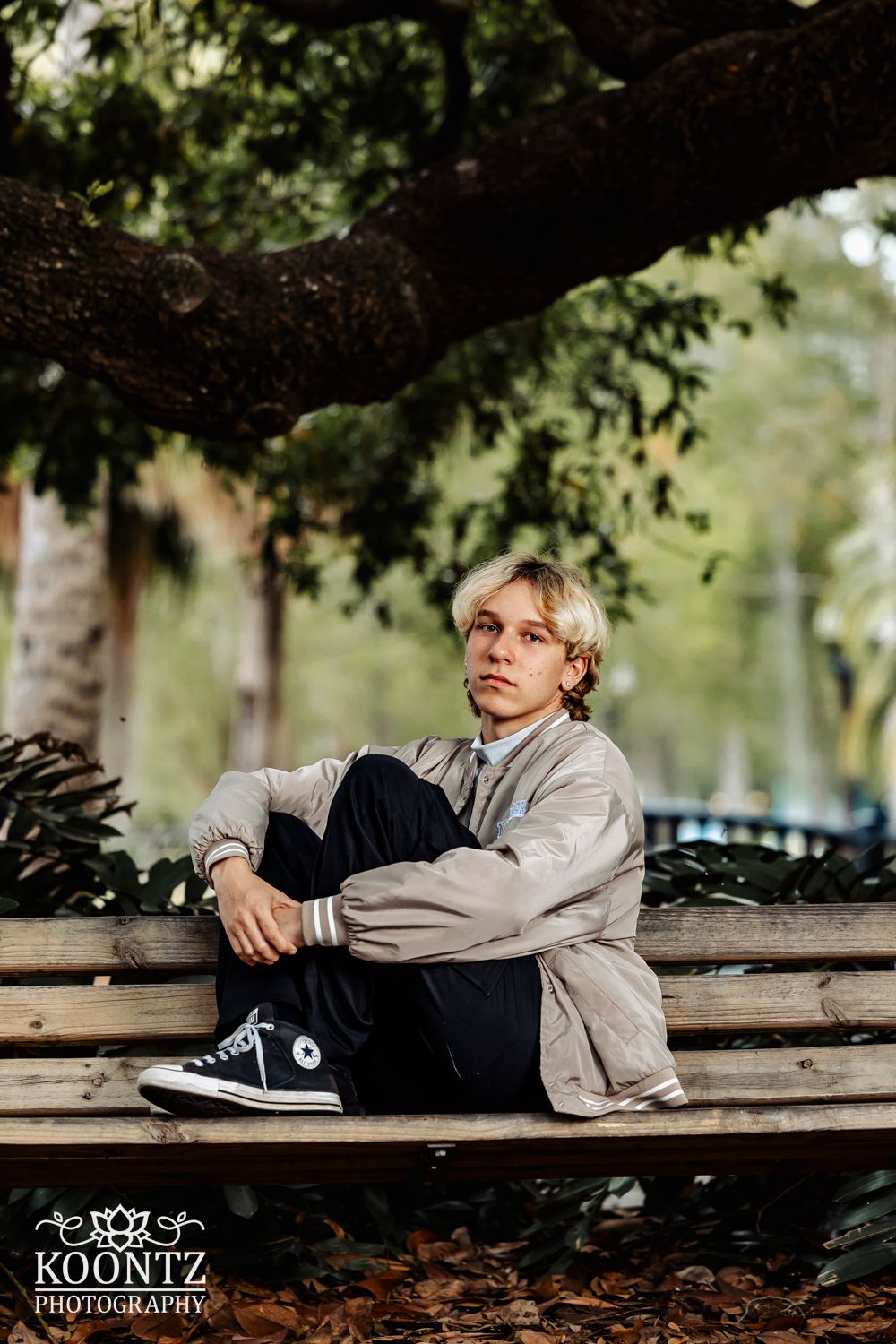 Artistic portrait on a wooden bench under sprawling tree branches.