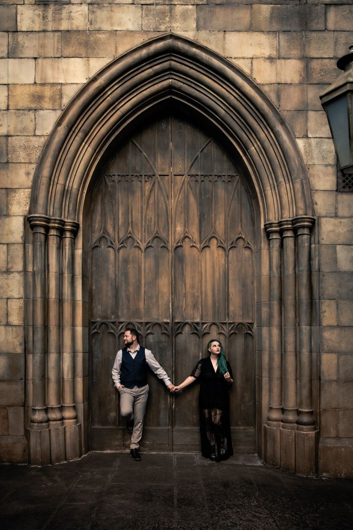 Couple holding hands before a grand gothic arched wooden door at Hogwarts castle.
