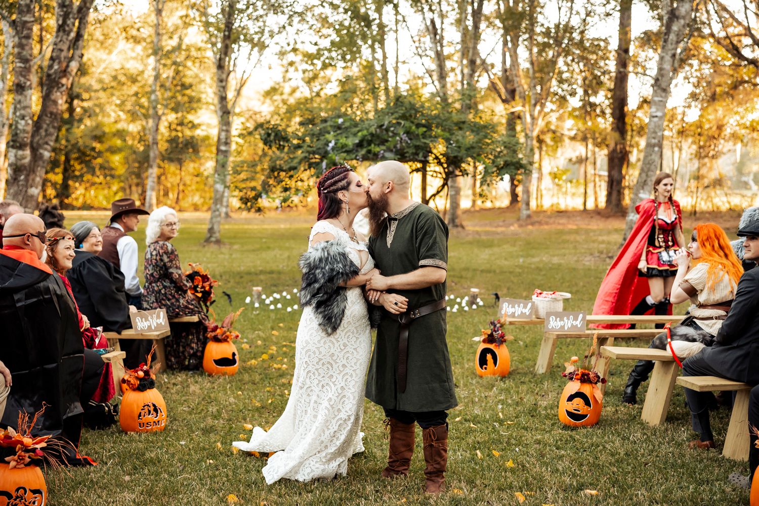 Outdoor fall wedding ceremony with guests seated among pumpkin decorations and autumn foliage.