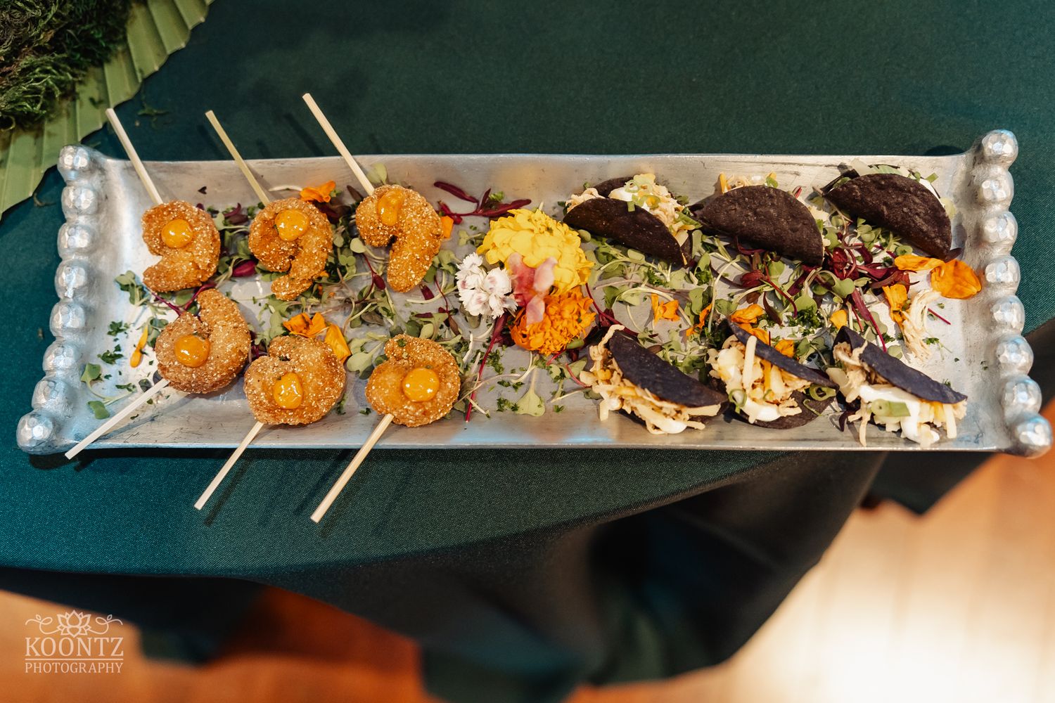 Gourmet appetizer platter featuring skewered items and dark garnishes on a pearl-trimmed tray.