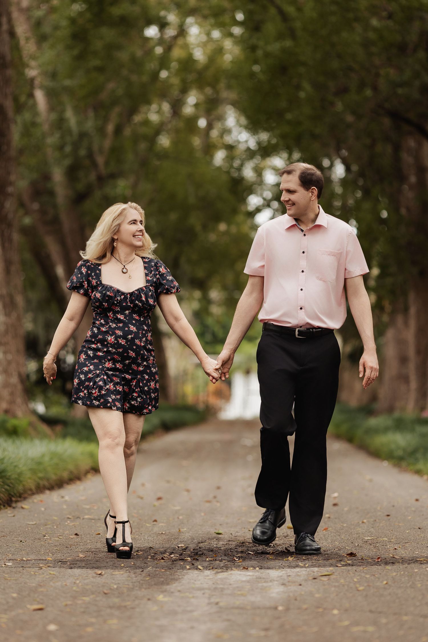 Happy couple holding hands and walking along a scenic tree-lined garden pathway together.