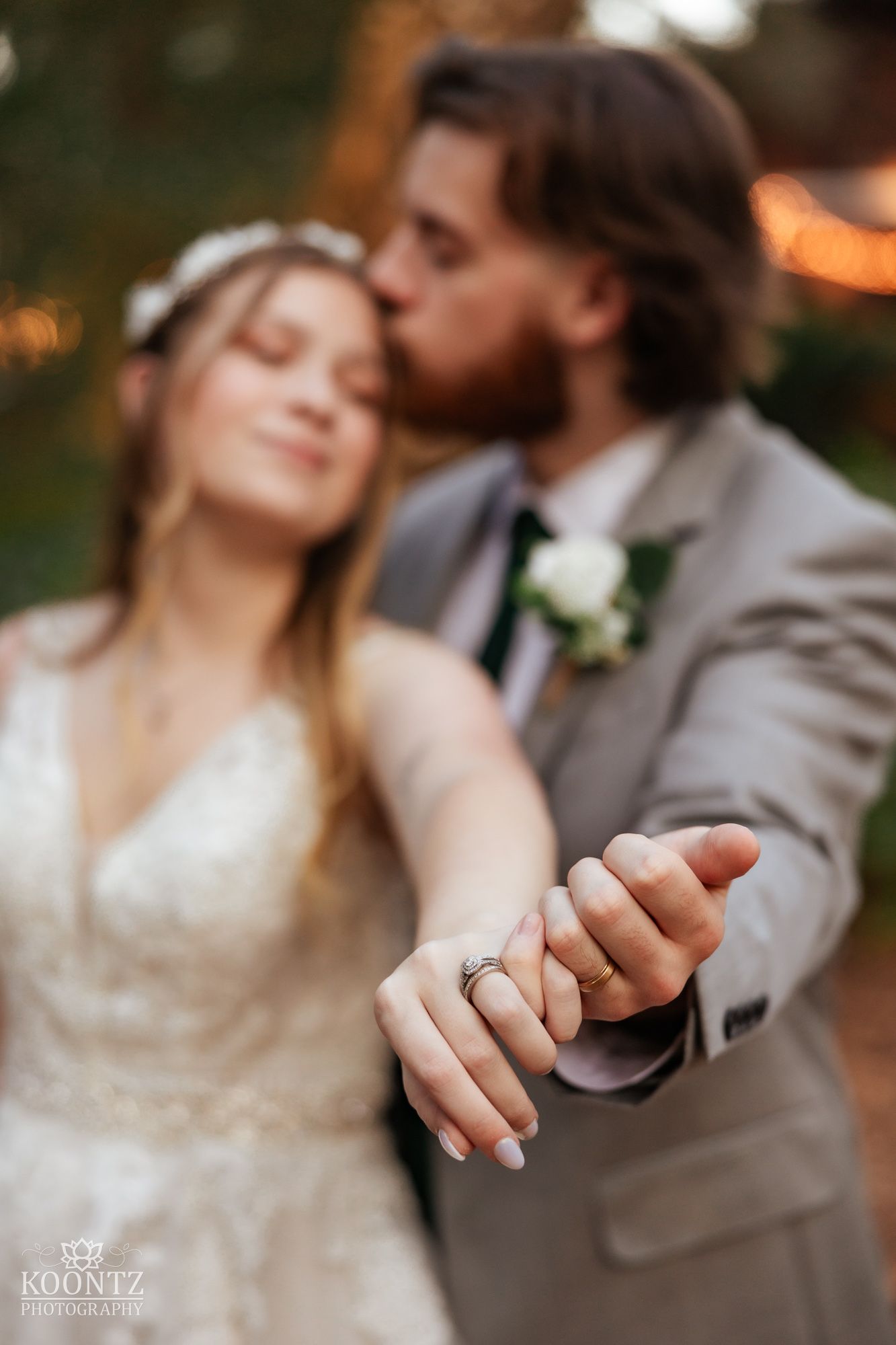 Close-up of bride and grooms wedding rings as groom kisses bride at romantic outdoor ceremony.