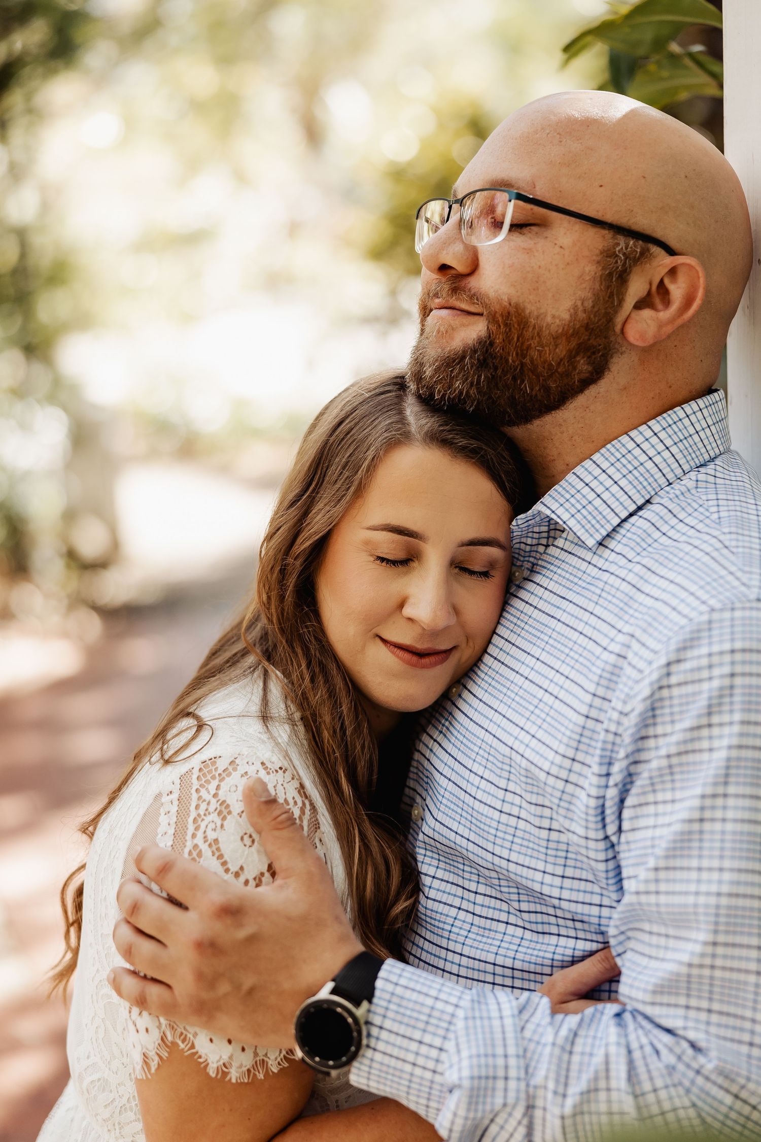 Couple sharing a tender embrace outdoors, woman resting head on mans chest with eyes closed peacefully.