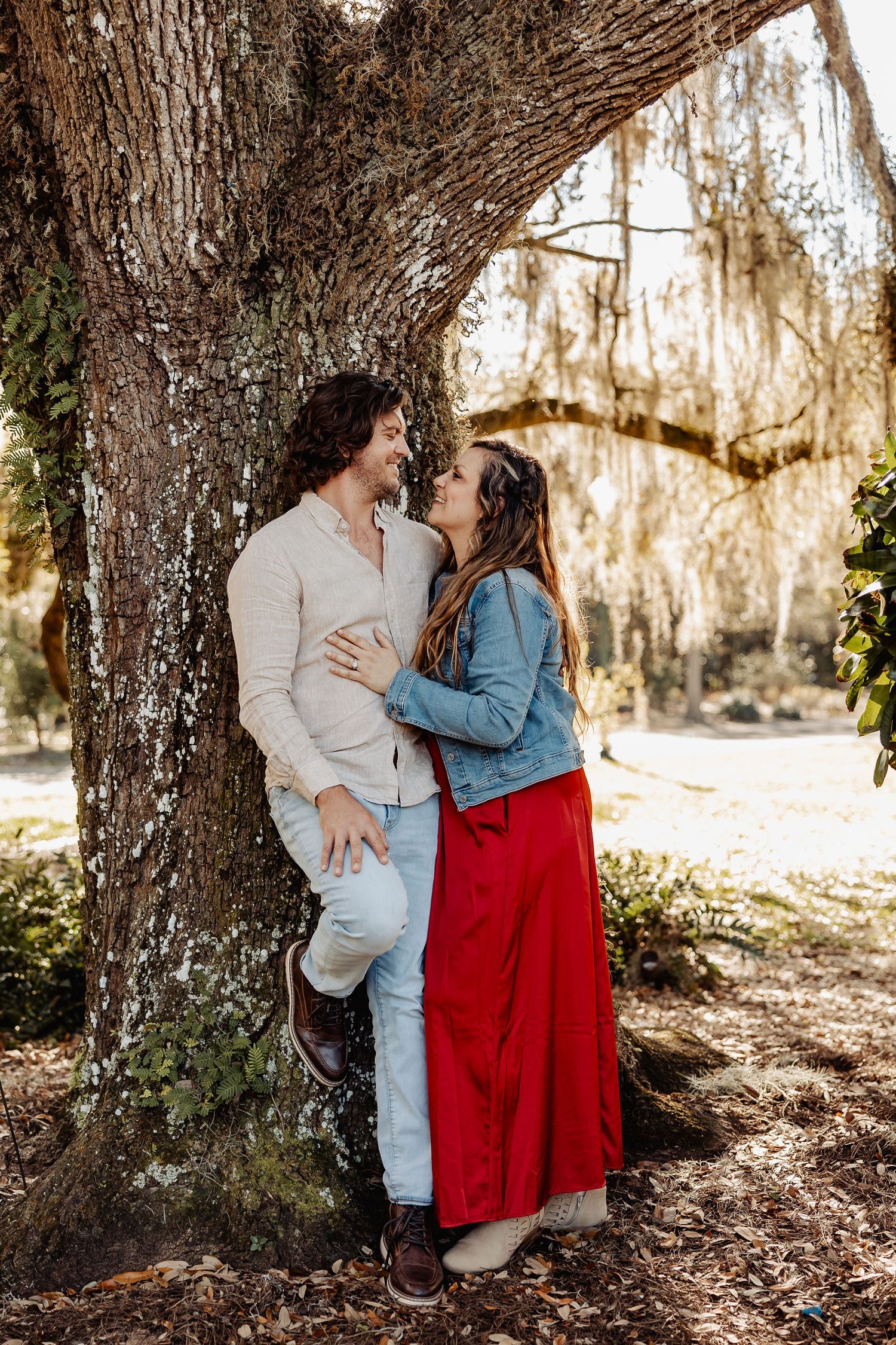 Couple sharing a romantic moment leaning against a large oak tree draped with Spanish moss.