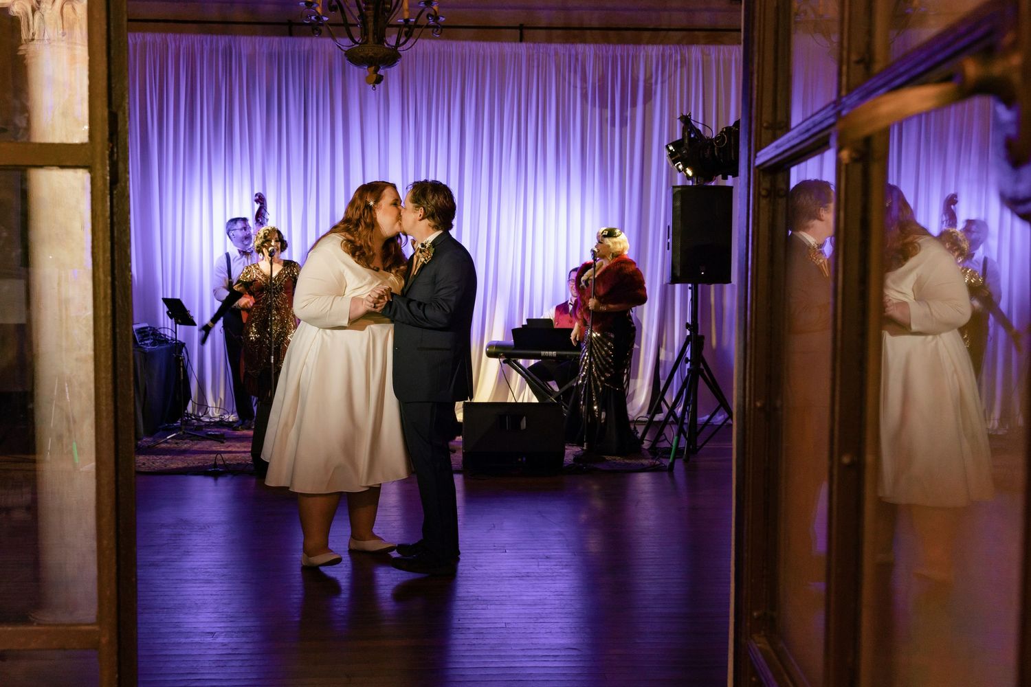 Bride and groom sharing romantic first dance kiss with live band performing in background.