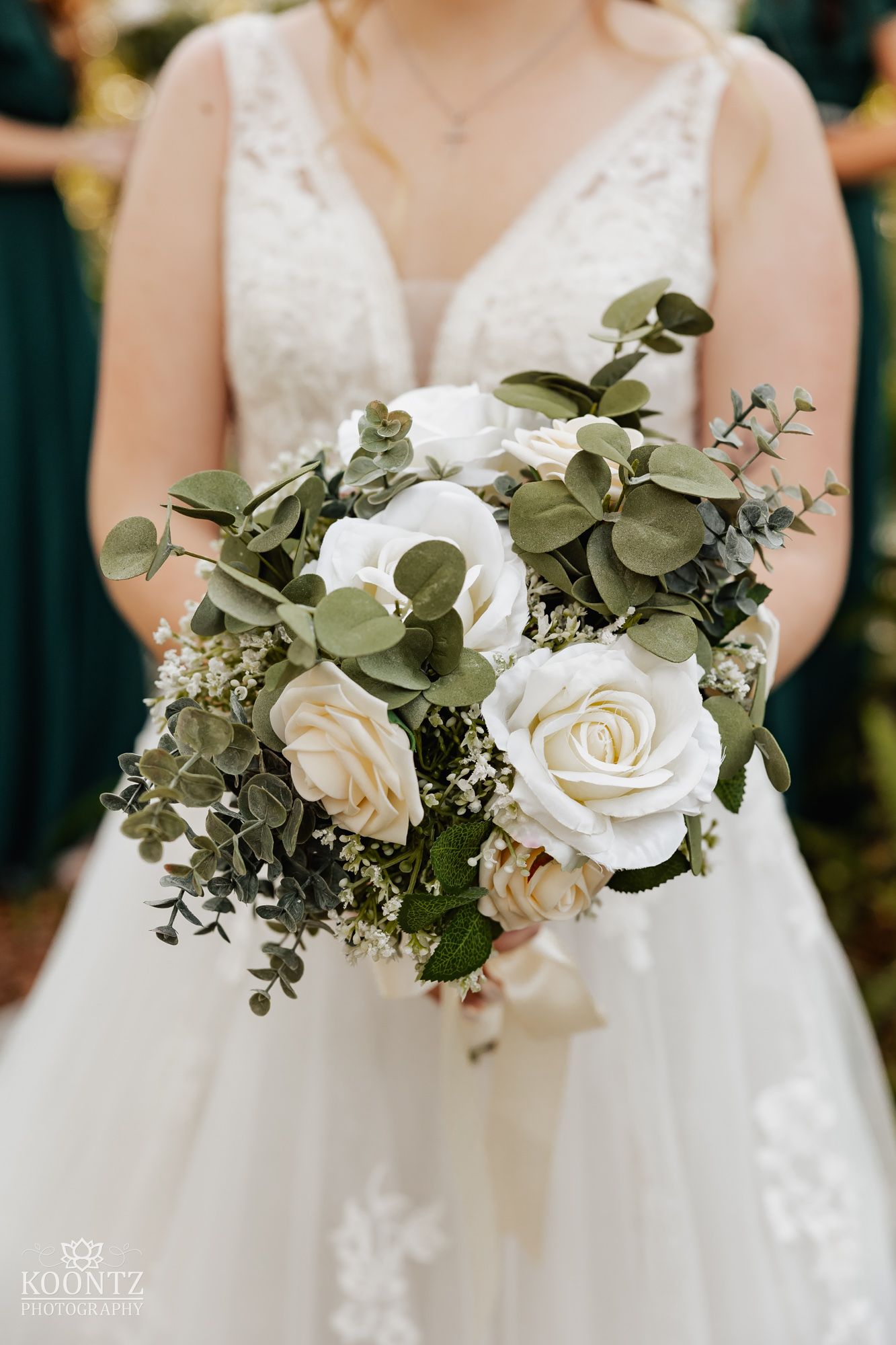 Bride holds a lush bouquet of white roses and eucalyptus greenery in a lace wedding gown.