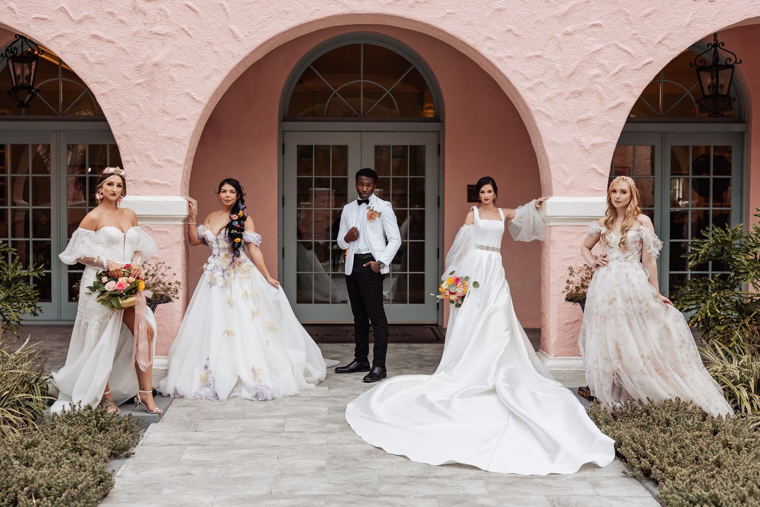 Four brides in white gowns flank a groom in a white tuxedo under a pink arched entrance.