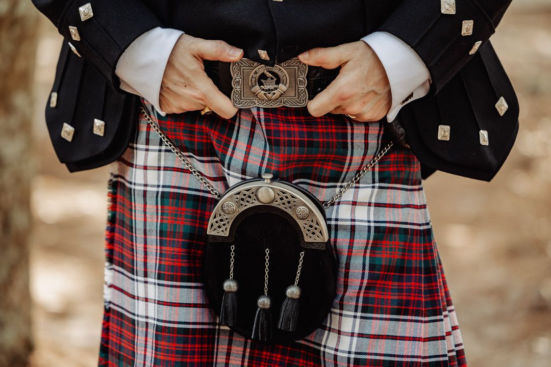 Detail shot of traditional Scottish kilt accessories including a decorative sporran against red tartan plaid.