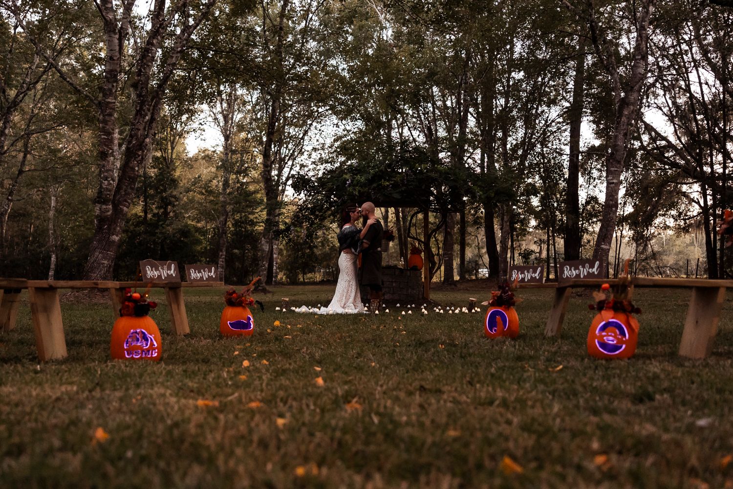A romantic wedding scene in an autumn forest with glowing pumpkins lining the path.