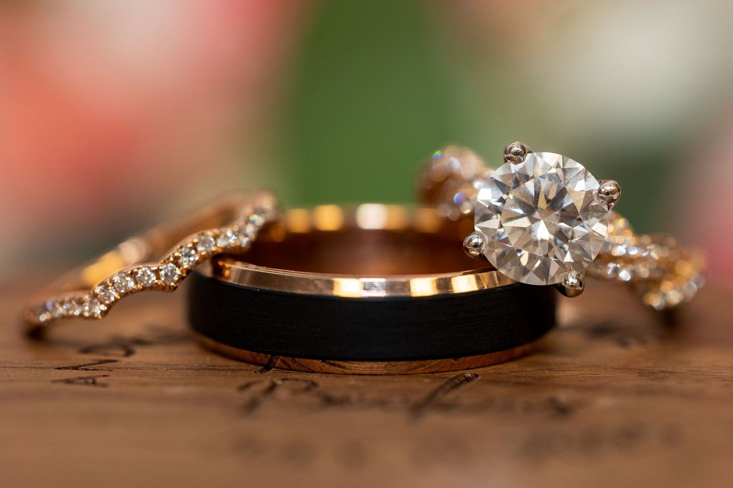 Three wedding rings including a black tungsten band, rose gold diamond band, and solitaire engagement ring.