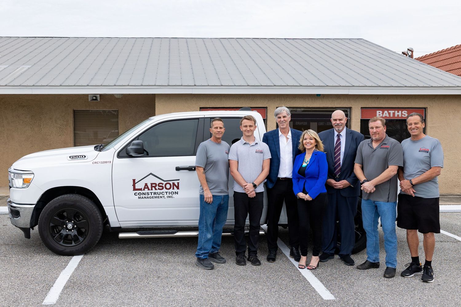 Larson Construction Management team of eight posing in front of a black company truck.