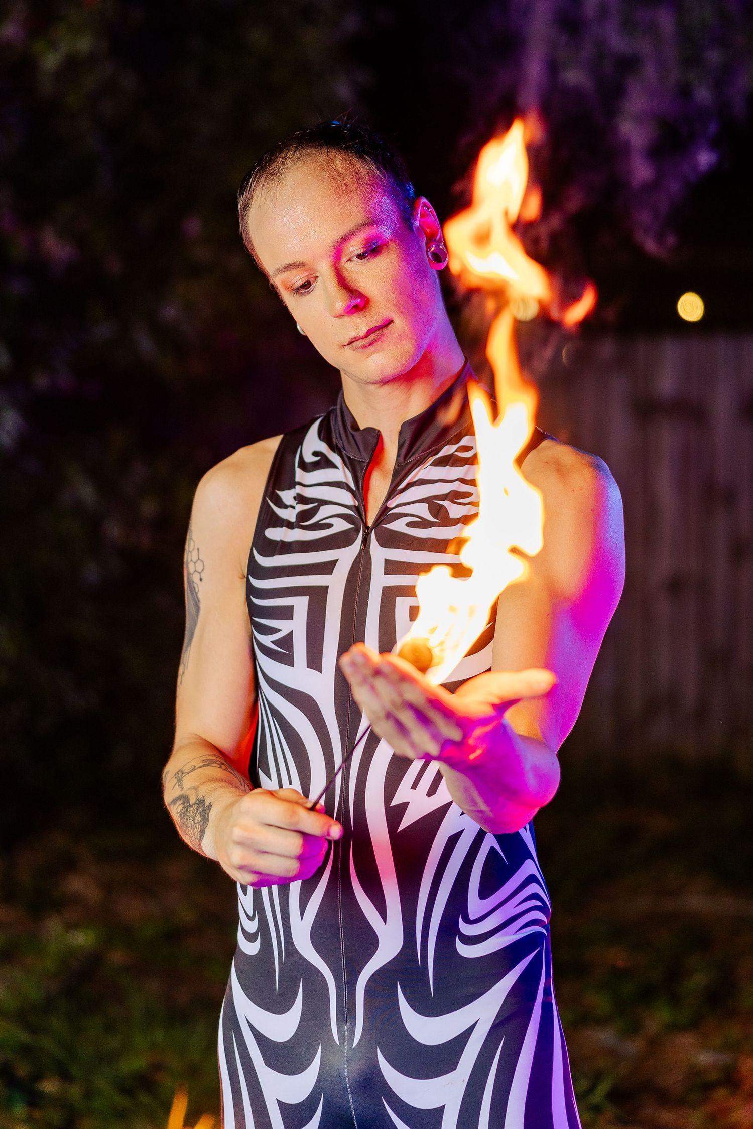 Circus artist in tribal costume manipulates fire with bare hands during a dramatic outdoor night show.