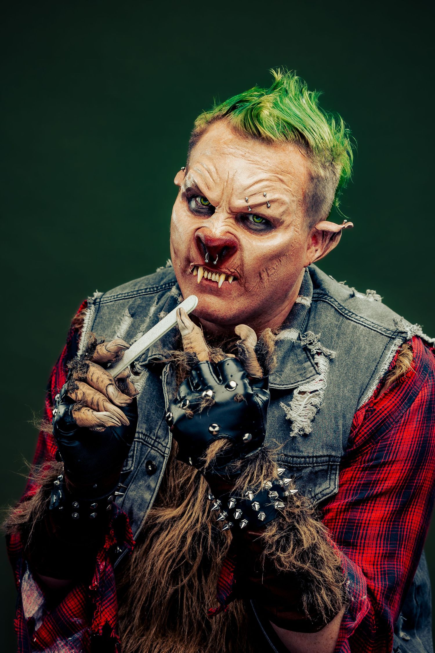 Creepy punk troll character with green mohawk, monster prosthetic makeup, and clawed hands holding a cigarette.