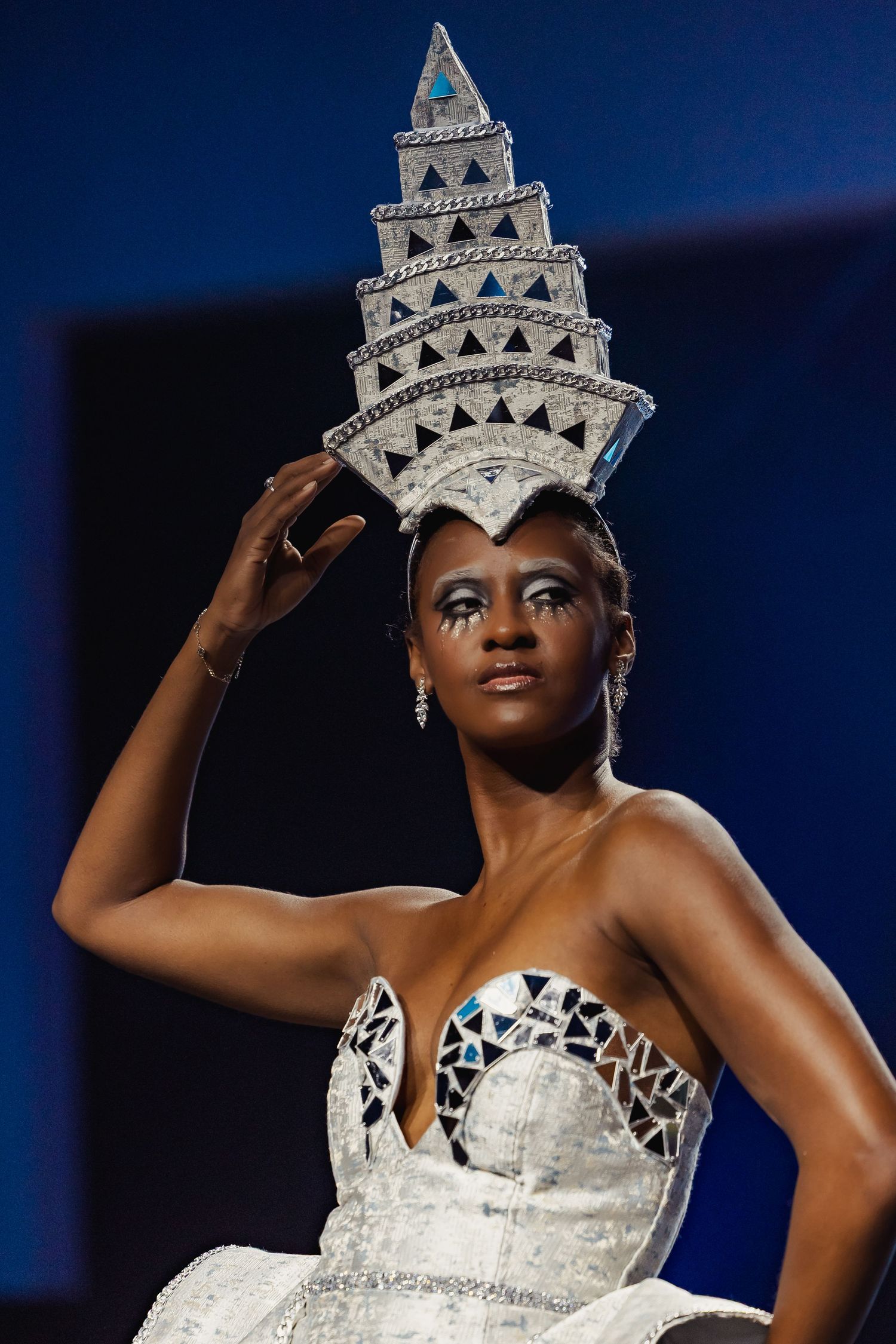 Close-up of model wearing ornate tiered geometric white crown and mosaic-detailed strapless gown.