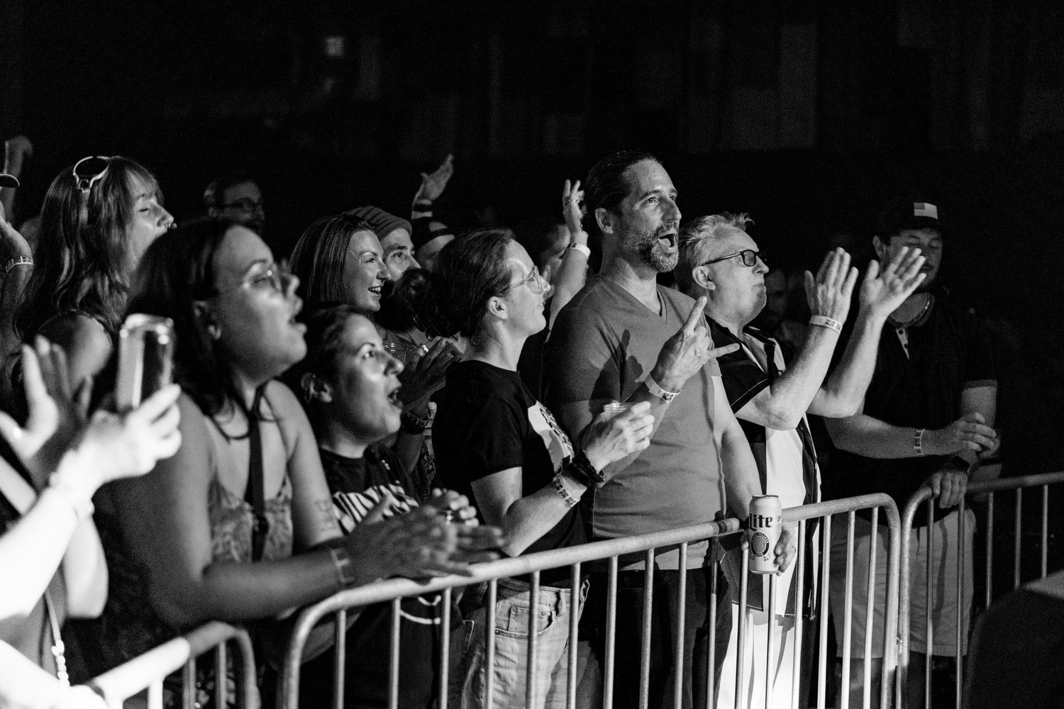 Enthusiastic concert crowd cheering behind a barrier at an outdoor music event in black and white.