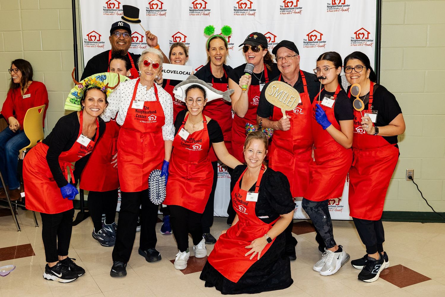 Team of volunteers in red aprons wearing fun costumes and accessories at a charity fundraiser event.