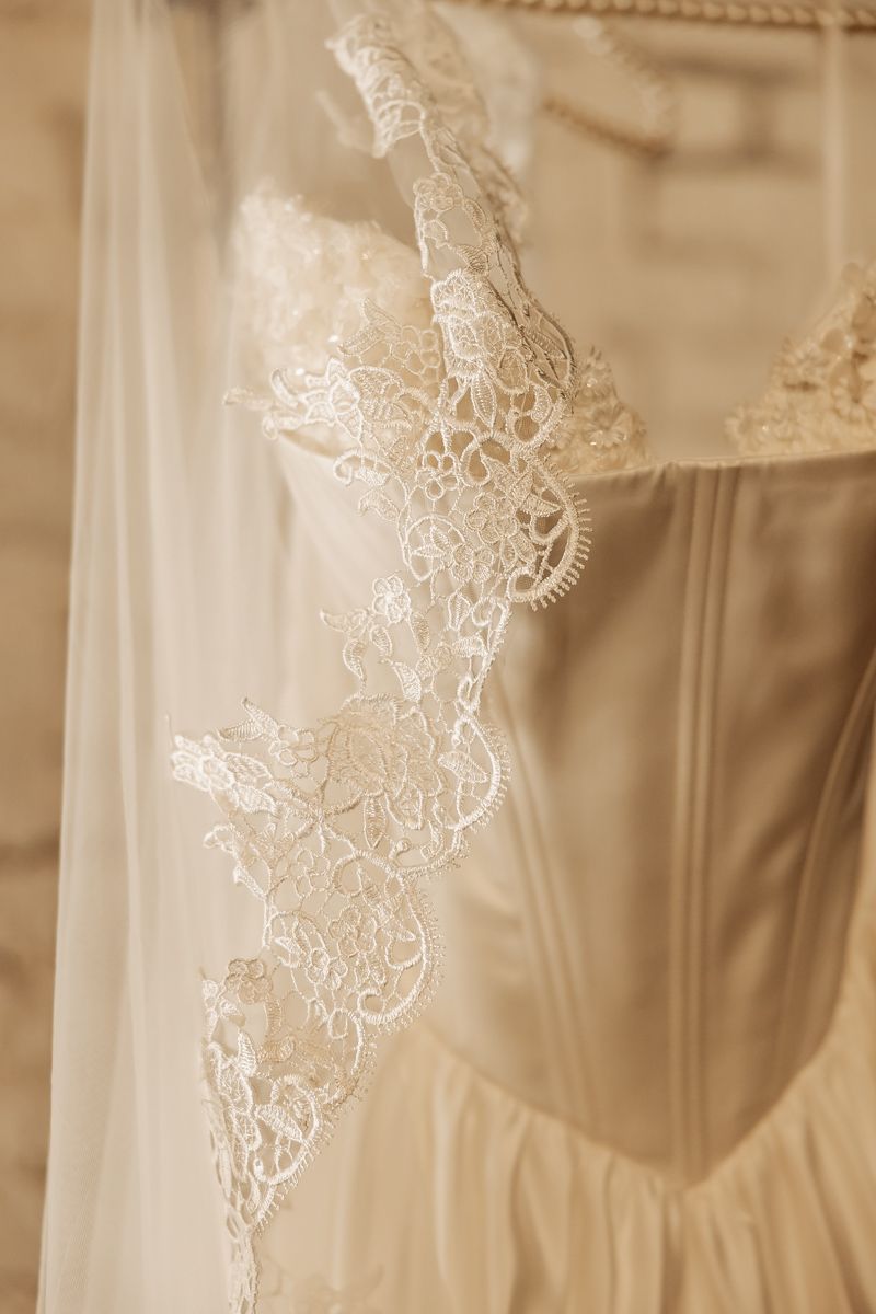 Close-up detail of elegant ivory lace wedding veil and corset bridal gown hanging together.