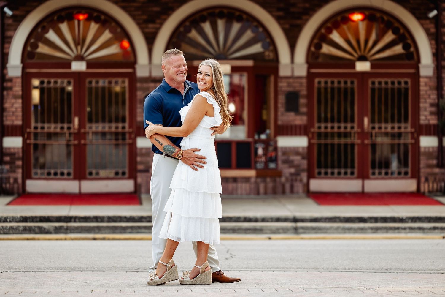 Smiling couple embracing in front of the red brick Athens Theatre arched facade.