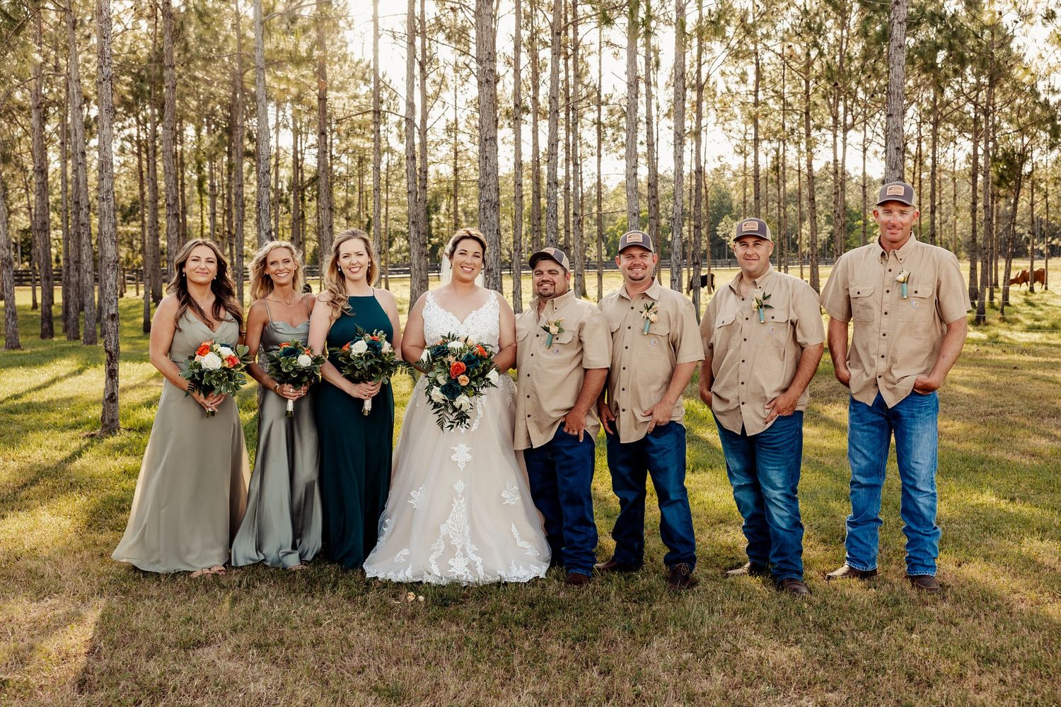 Wedding group photo in a pine forest with bridesmaids in neutral dresses and groomsmen in casual attire.