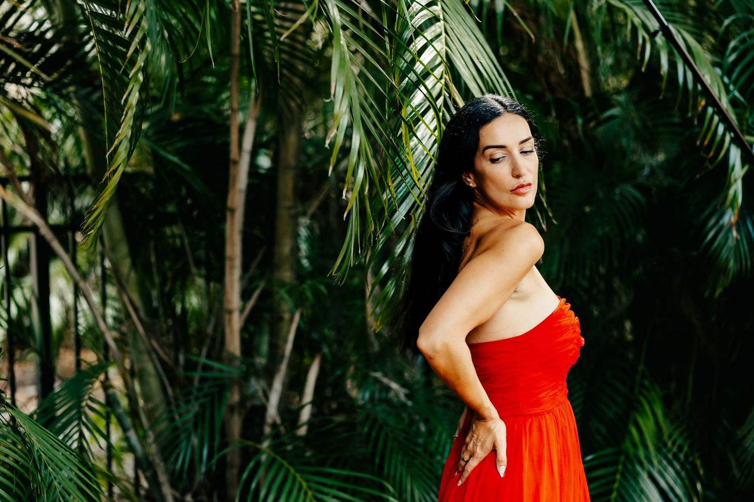 Side profile portrait shot with vibrant red dress against green palm leaves.