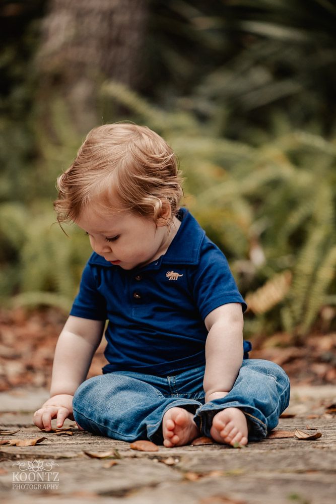 Small child in navy blue polo shirt sitting on wooden surface looking downward.