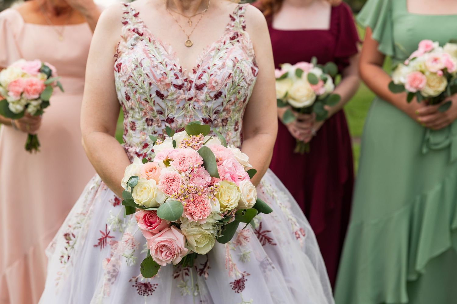 Close-up of bride holding pink and white rose bouquet wearing floral embroidered wedding gown.
