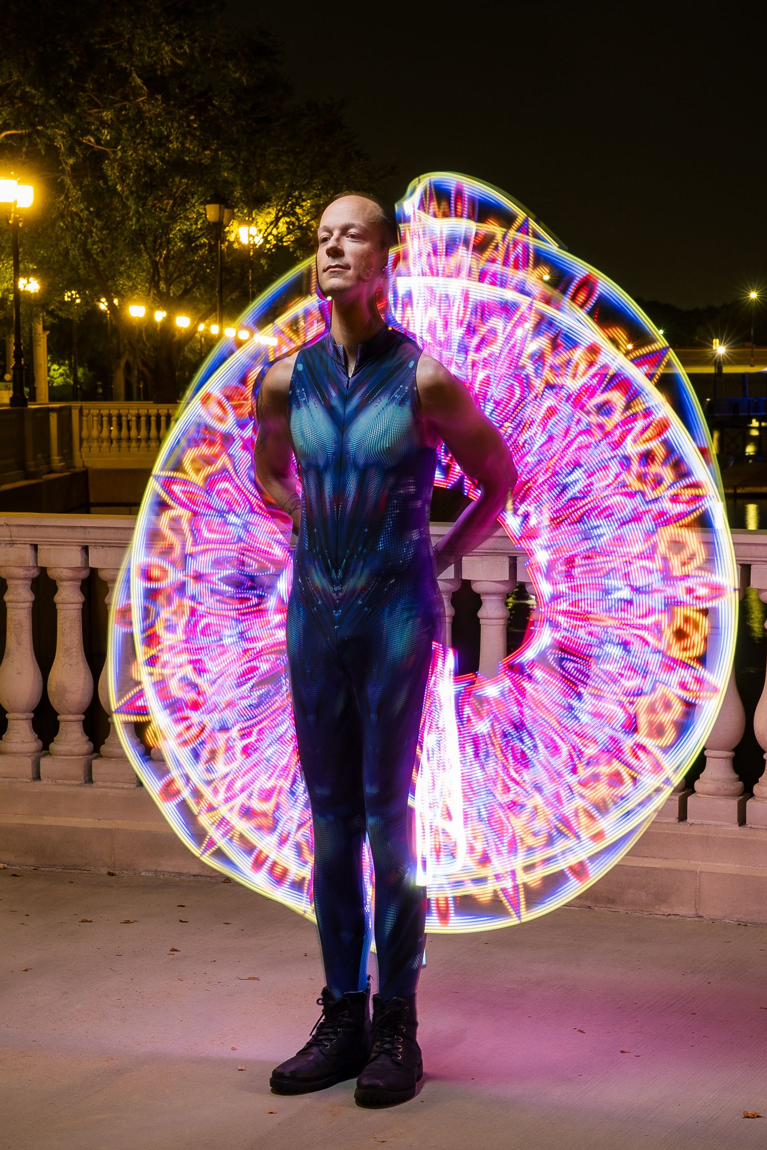 Person in blue bodysuit stands with stunning circular mandala light painting glowing behind them at night.
