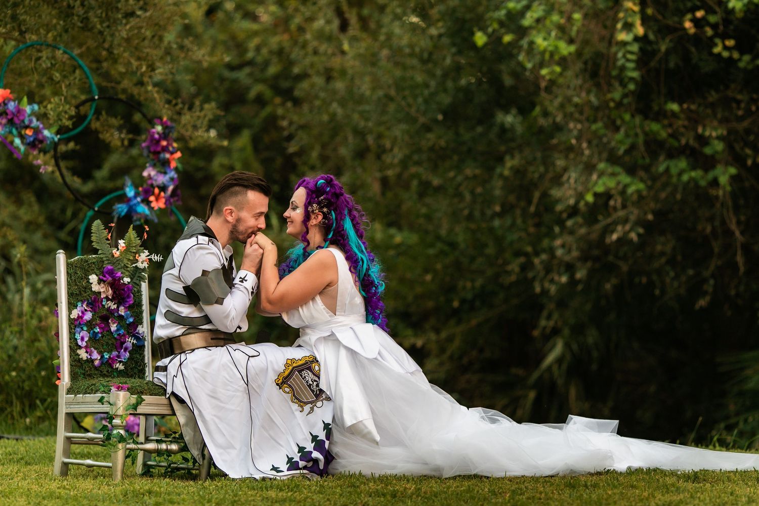 Bride and groom share a romantic moment seated outdoors, surrounded by colorful floral decorations at their wedding ceremony.